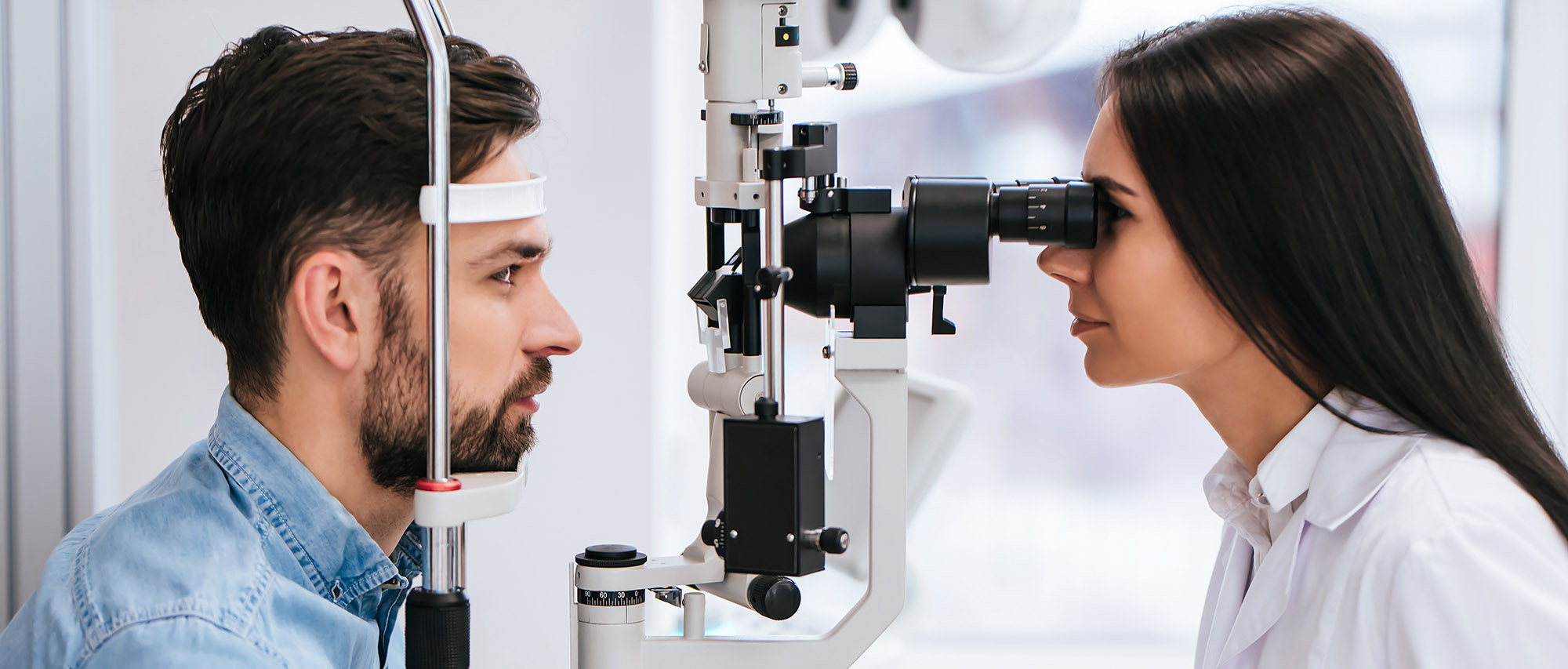 Attractive female doctor  ophthalmologist is checking the eye vision of handsome young man in modern clinic. Doctor and patient in ophthalmology clinic.