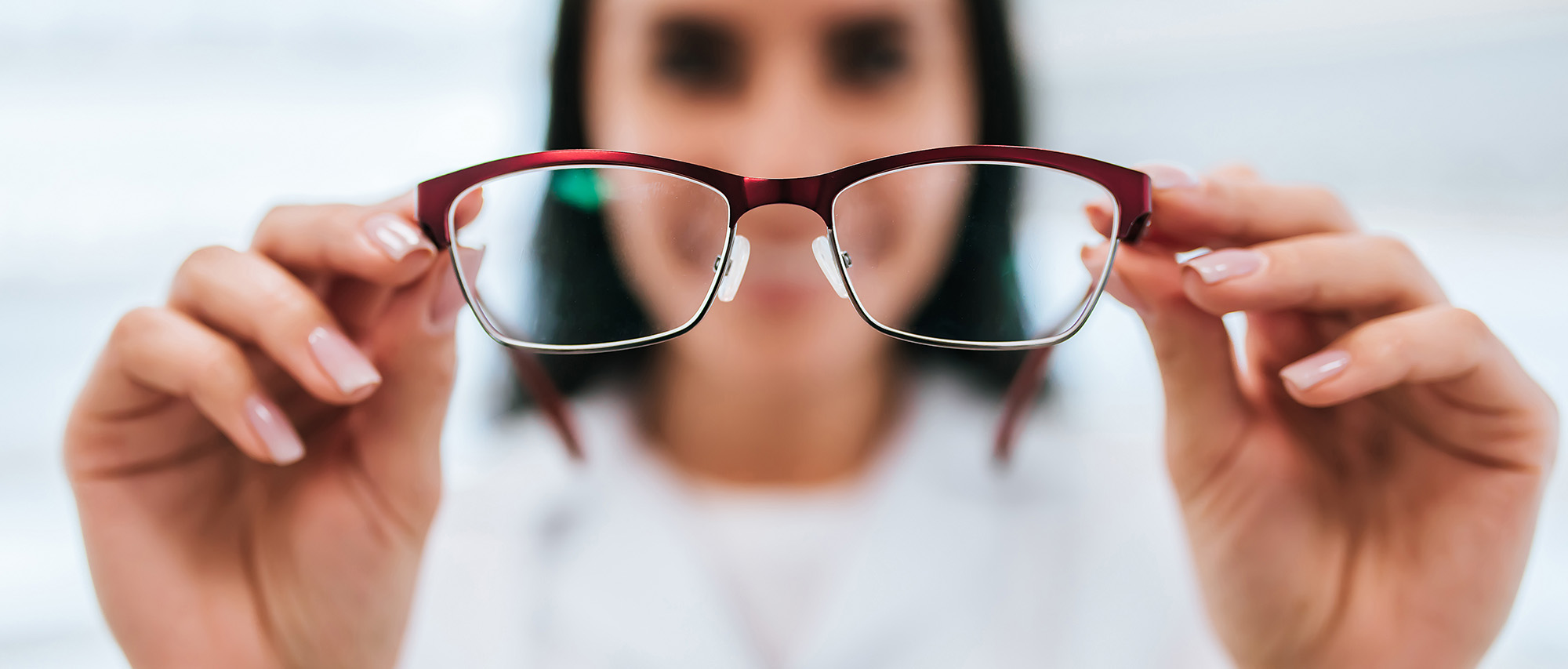 Cropped image of attractive young female doctor in ophthalmology clinic. Doctor ophthalmologist is standing near shelves with different eyeglasses.